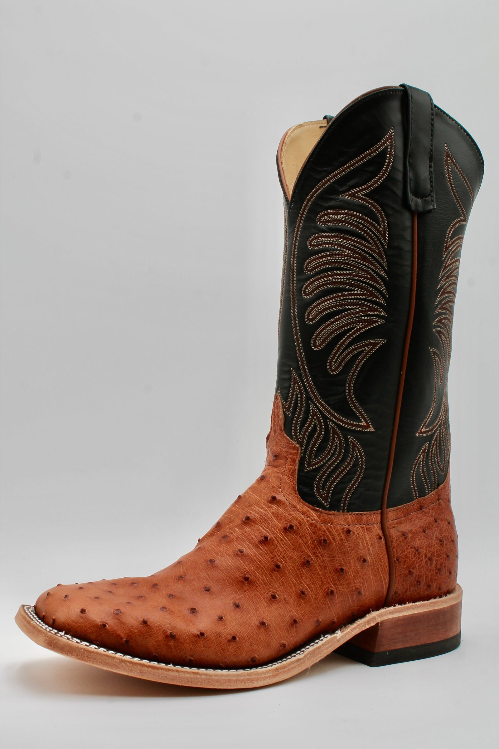 Brown and black cowboy boot with intricate stitching on a gray background